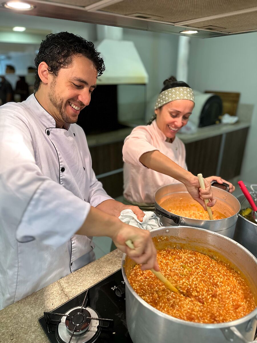 Jackson e Camila sorrindo enquanto mexem risoto em duas panelas grandes